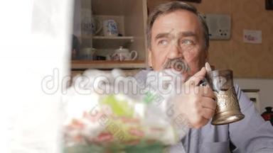 有胡子的老人端着一杯热饮和饮料。 他坐在窗边，在家<strong>吃早饭</strong>